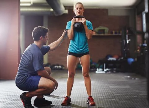 Helping to perfect her form. a trainer helping a young woman lifting kettlebells Stock Photos