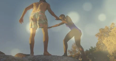 Helping shirtless man in patterned trunks pulling woman in purple swimsuit up Stock Footage 331635046