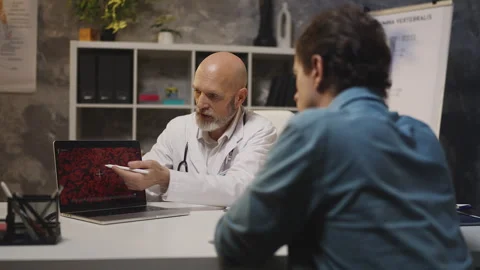 Hematologist explains blood test results on laptop to male patient in clinic Stock Footage 342749632