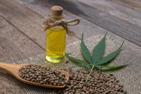 Hemp oil in a glass bottle tied with a bow Hemp seeds in a wooden spoon on th Stock Photos