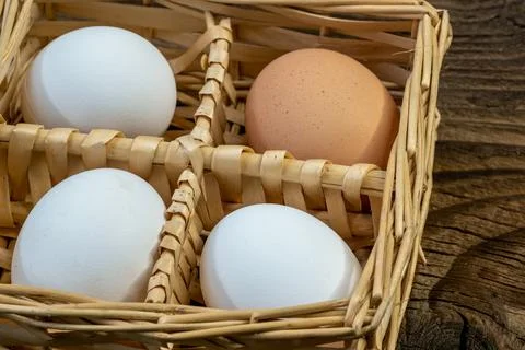 Hen Eggs in a wicker basket on an old vintage planked wood table. Rural kit.. Stock Photos