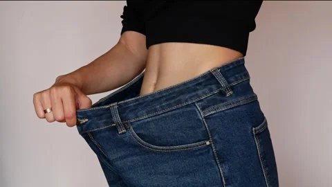 Her flat stomach and slim waist are lost in oversized jeans. Stock Footage 308398394