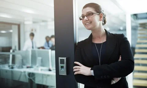 Her office runs like clockwork. a young businesswoman standing with her arms Stock Photos