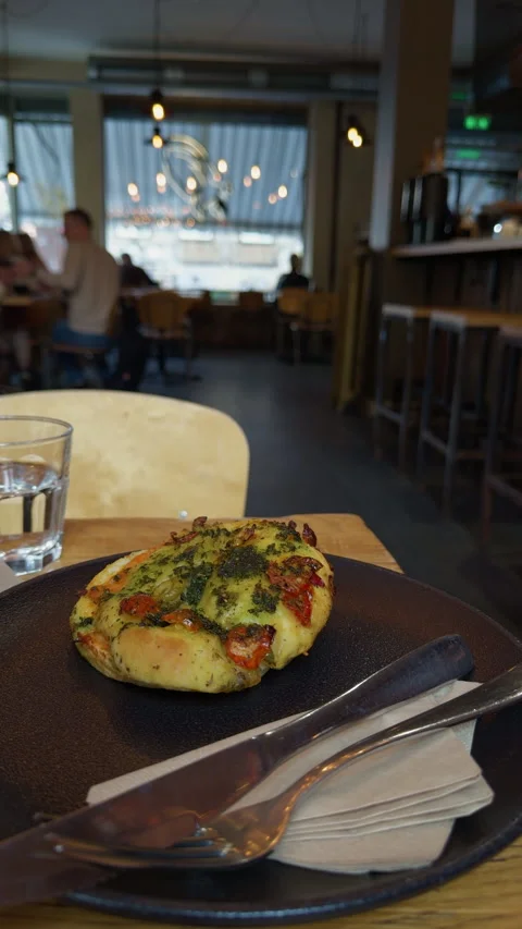 Herb topped baked flatbread served on dark plate beside cutlery and water glass Stock Footage 345126494