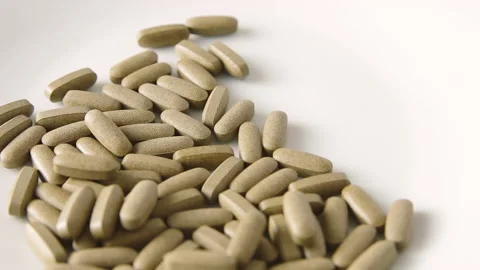 Herbal medicine tablets fall onto a white plate. Concept for self-medication Stock Footage 130409658