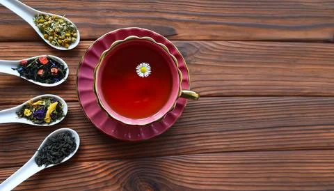 Herbal tea in a red cup with assorted loose leaves on wooden spoons. A top-down Stock Photos