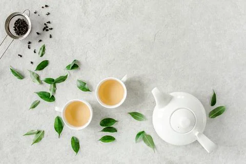 Herbal tea with two white tea cups and teapot, with green tea leaves. Flat lay Stock Photos