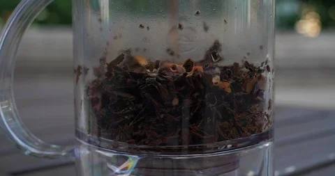 Herbs inside a tea maker as a warm tea is slowly being prepared and stirred Stock Footage 100338819