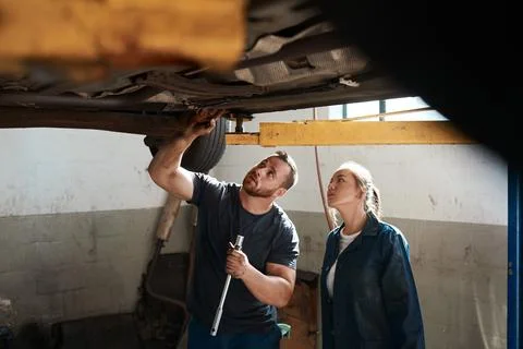Heres where the problem lies. two mechanics working together under a lifted car. Stock Photos