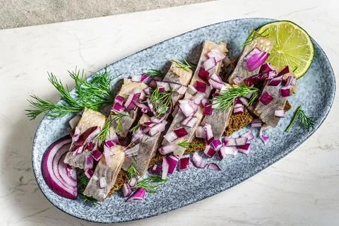 Herring fillets on rye bread, garnished with red onion, dill and lemon 스톡 사진