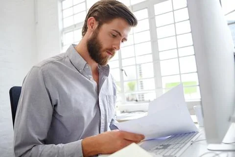 Hes the admin master. a young designer holding paperwork while sitting in front Stock Photos