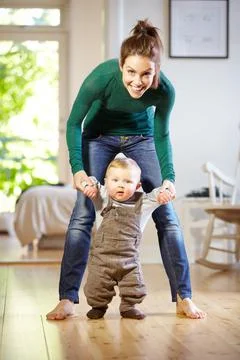 Hes learning so fast. Smiling young mom helping her baby boy learn to walk. Stock Photos