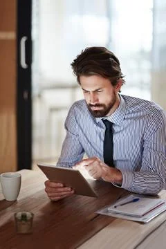 Hes a tech savvy exec. a young businessman using a digital tablet in an office. Stock Photos