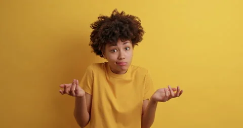 Hesitant clueless dark skinned young Afro American woman spreads palms feels Stock Footage 149914267