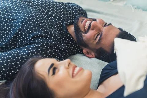 Heterosexual interracial couple lying down on bed. Happy relationship concept Stock Photos