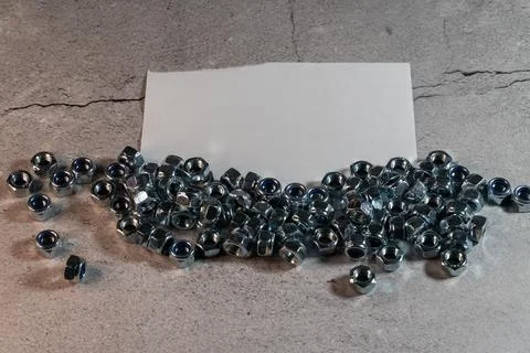 Hex nuts with blue nylon inserts scattered on gray background with blank card Stock Photos