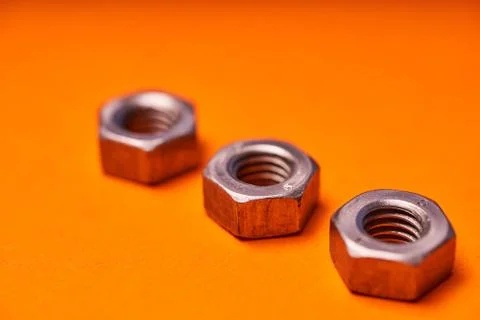 Hex nuts on orange background. Bolted connection elements Stock Photos