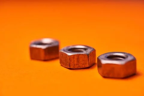 Hex nuts on orange background. Bolted connection elements Stock Photos