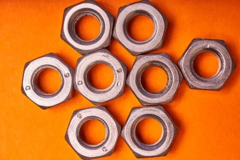 Hex nuts on orange background. Bolted connection elements Stock Photos