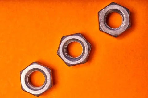 Hex nuts on orange background. Bolted connection elements Stock Photos