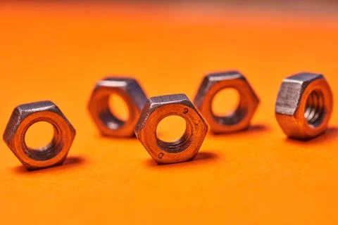 Hex nuts on orange background. Bolted connection elements Stock Photos