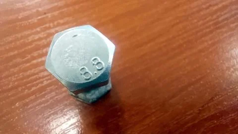 Hexagonal bolt resting on a wooden table displays detailed markings and ref.. Stock Photos