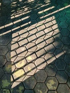 Hexagonal concrete paving block texture with dramatic fence shadows. Stock Photos