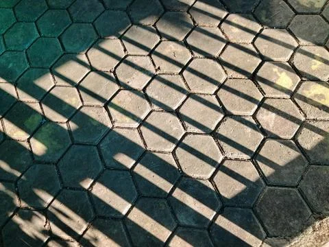 Hexagonal concrete paving block texture with dramatic fence shadows. Stock Photos