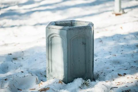 Hexagonal concrete waste bin standing in a park, surrounded by fresh white .. Stock Photos
