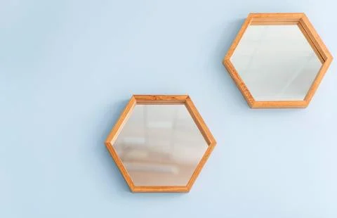Hexagonal mirrors with wooden frames are mounted on a light blue wall, creating Stock Photos