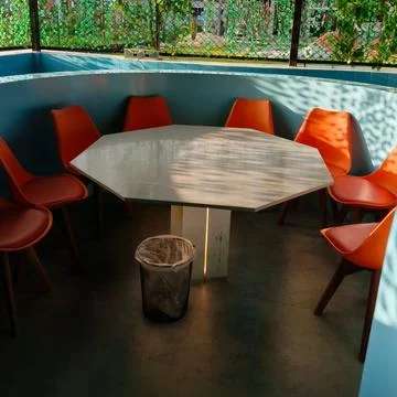 Hexagonal table and orange chairs sit Stock Photos