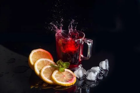 Hibiscus cold tea splash from the fallen ice cube into glass with beverage is Stock Photos