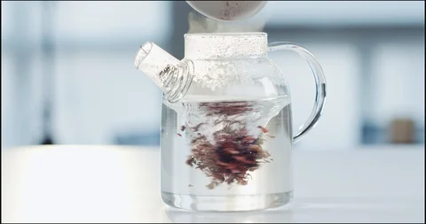 Hibiscus tea being dropped for brew into a glass teapot with hot water whirlpool Видео 101606294