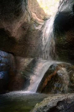 Hidden cave waterfall cascading down mossy canyon rocks in morning sun 库存照片