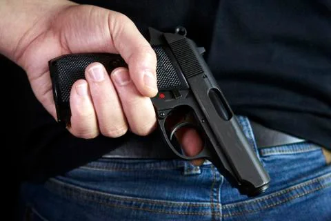 Hidden gun in hands back side to man in blue jeans Stock Photos