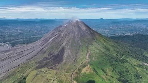 From high above, Sinabung dominates the landscape, a solitary giant rising from Stock Footage 328207375
