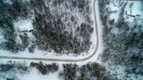High Aerial View of Sharp Curve on Snowy Dirt Road and Winter Houses Foto stock