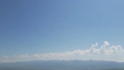 A high-altitude view of distant, snow-capped mountains beneath a vast blue sky Stock Footage 334541829