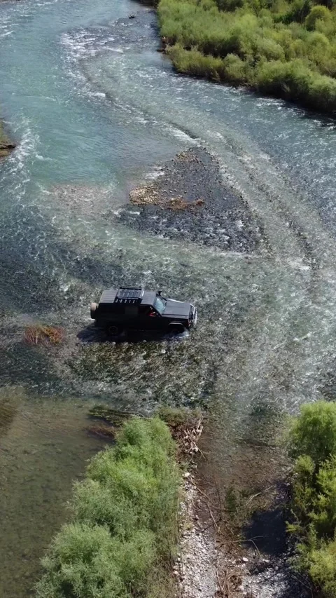 High angle aerial view of 4x4 off-road vehicle navigating through river Vídeos de archivo 336690768