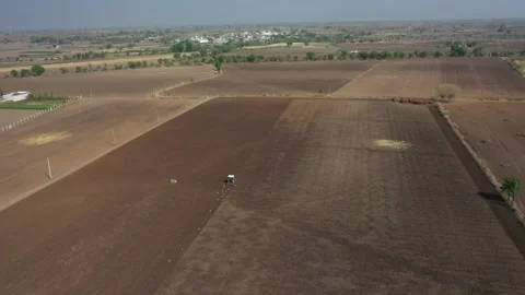 High-angle aerial view of a blue tractor cultivating a vast patch of brown Stock Footage 336813615