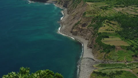 High-Angle Aerial View of a Rugged Rocky Coastline with a Pebble Beach, Blue Видео 335006173