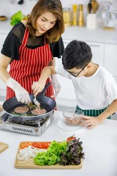 High angle of Asian boy making patties on hot pan near woman in apron while.. Foto stock