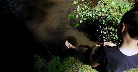 High angle boy on riverbank splashing feet in river Stock Footage 116046802