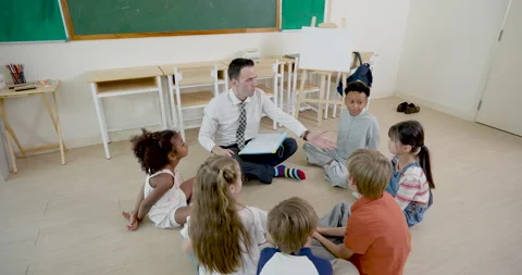 High angle classroom view follows male adult teacher guiding young multicultural Stock Footage 341933751