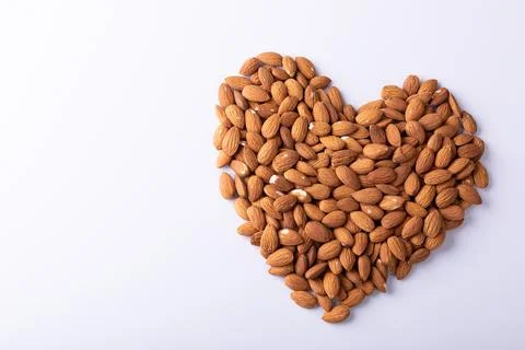 High angle close-up of almonds arranged in heart shape pattern on wooden white Fotos de archivo