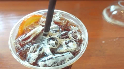 High-angle close-up of iced black coffee with a fresh orange slice. Видео 339781259