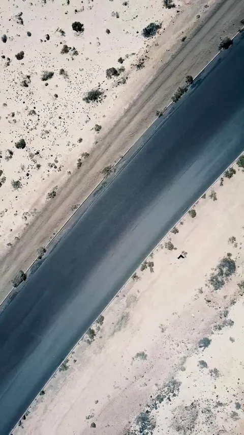 High-angle drone perspective following a solitary black car driving along an Stockbeeldmateriaal 344846178