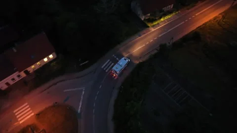 High angle drone shot a camper van driving through a illuminated town, night Stock Footage 317673808