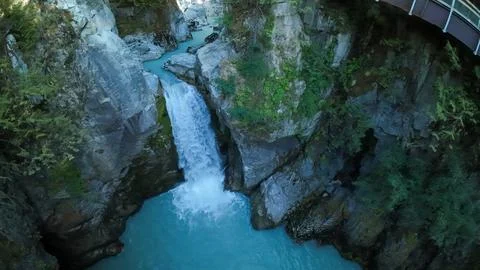 High angle drone shot looking into a deep rock canyon as a waterfall plunges Foto stock