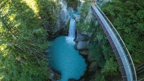 High angle drone shot over a curved canyon pedestrian bridge and a waterfall Foto stock